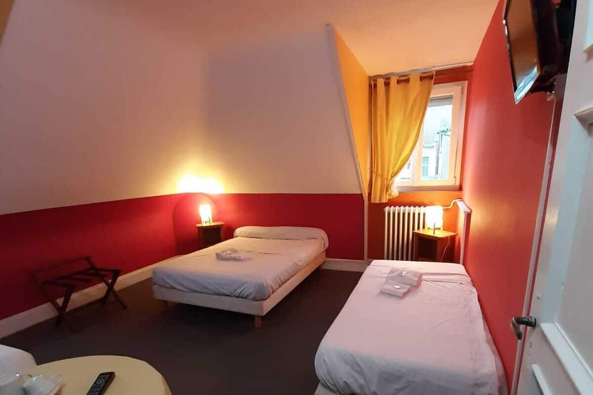 A hotel room with two single beds, a small table with a remote control, and a television mounted on the wall.