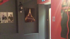 A hallway with a dark wall, a framed picture of the Eiffel Tower, and a red wall with a no-smoking sign. - Hotel du Cygne (Beauvais)