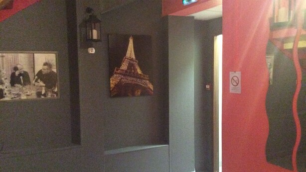 A hallway with a dark wall, a framed picture of the Eiffel Tower, and a red wall with a no-smoking sign. - Hotel du Cygne (Beauvais)