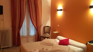 A hotel room with a bed, a chair, a radiator, and a window with curtains. - Hotel du Cygne (Beauvais)