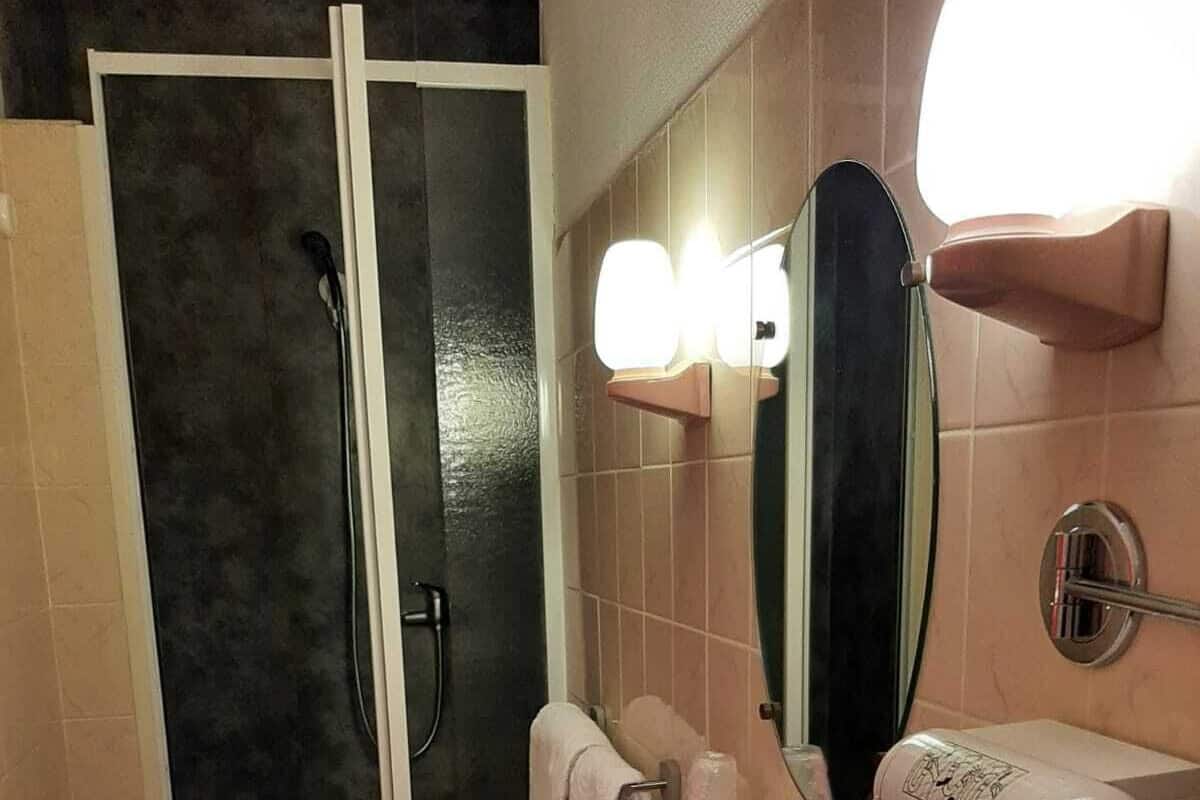A bathroom with a glass shower door, a sink with a mirror, and a towel rack.