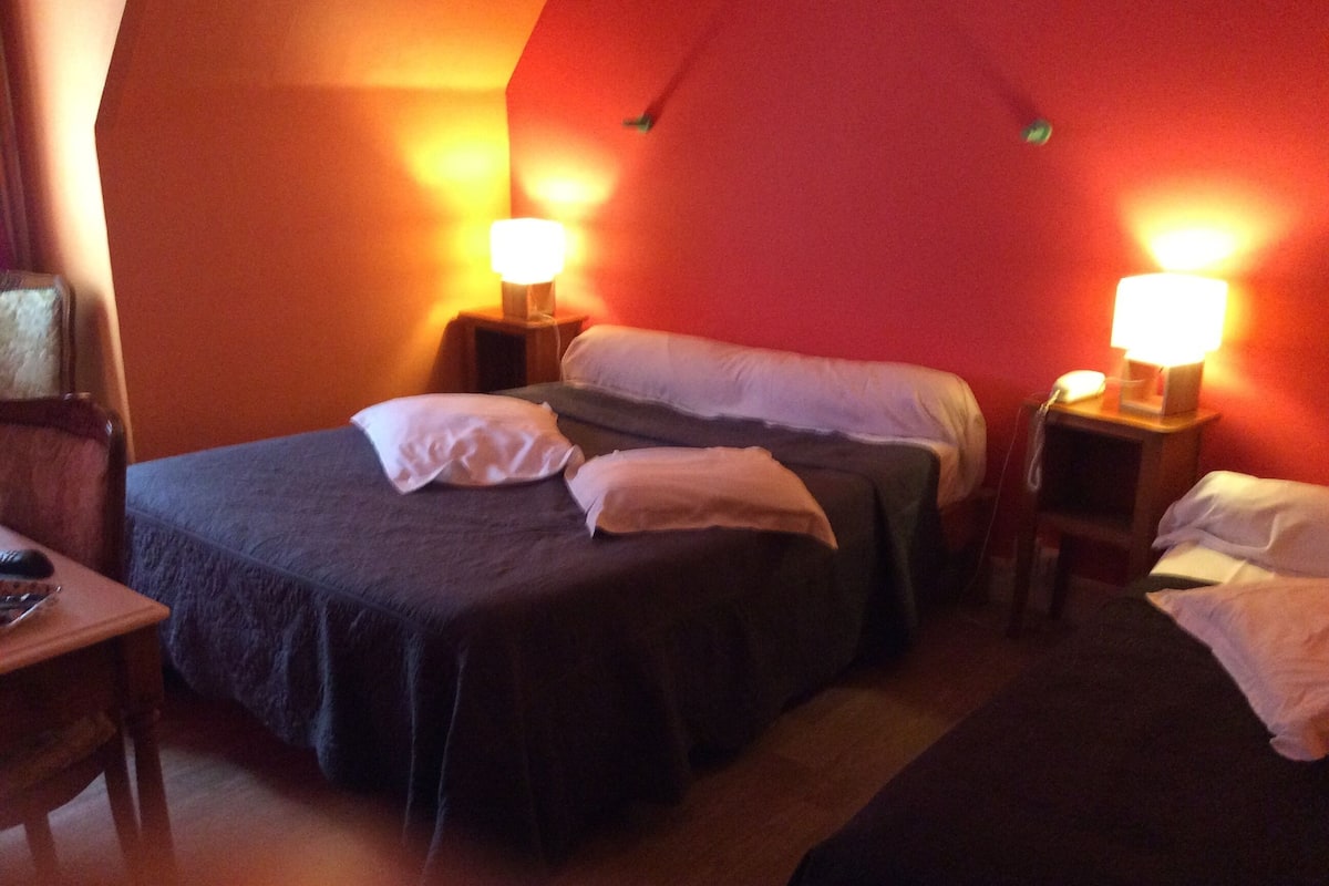 A room with two beds, each with a pillow and a bedside table with a lamp.
