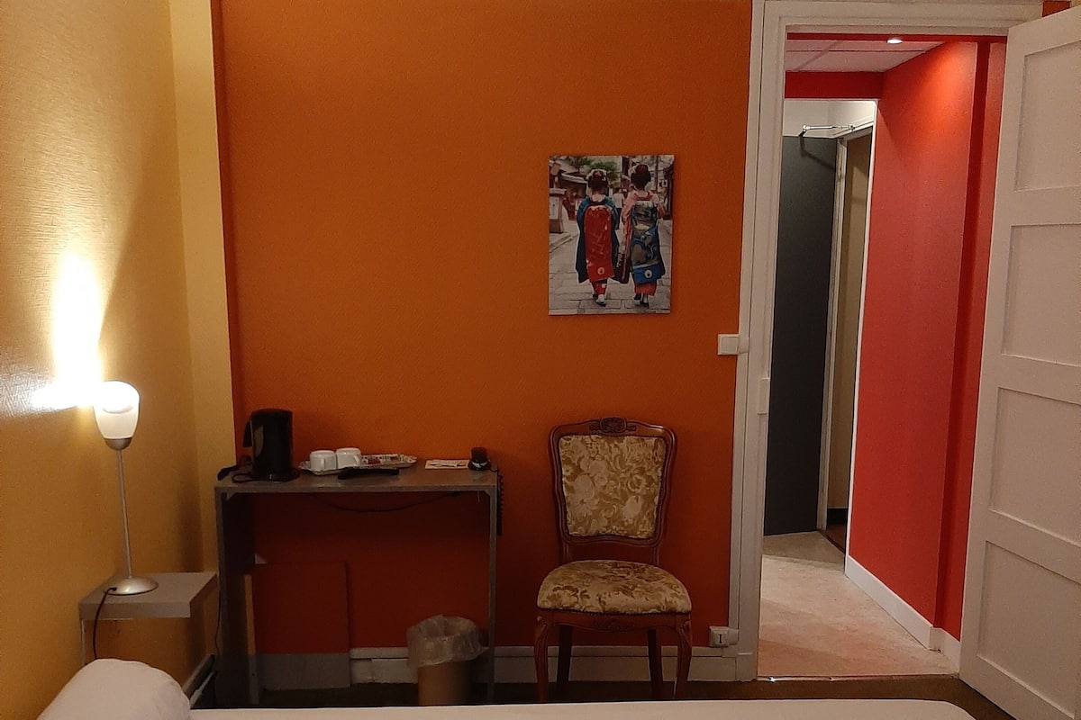 A hotel room with a bed, a desk with a chair, a lamp, and a painting on the wall.