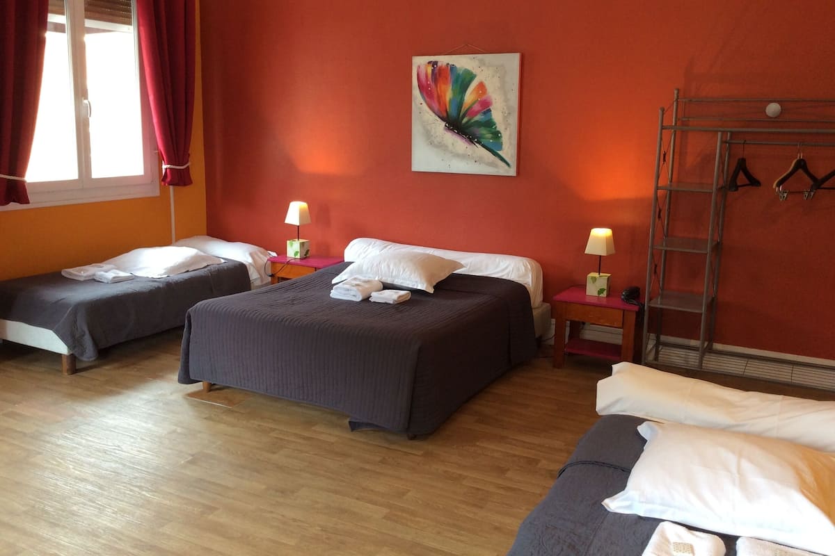 A hotel room with two single beds, a wooden floor, a red accent wall, a painting, a ladder, and a coat rack.