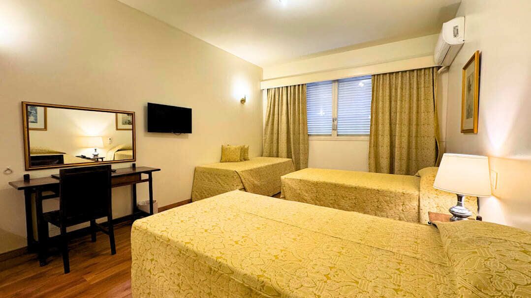 A hotel room with a desk, two single beds, a television, and a window with curtains.