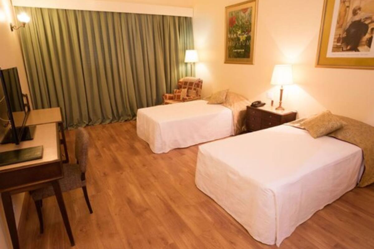 Hotellihuone, jossa on kaksi erillistä sänkyä, työpöytä, tuoli, lamppu ja verho.