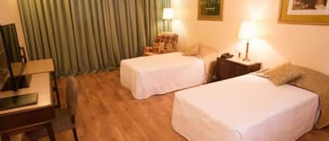 A hotel room with two single beds, a desk, a chair, a lamp, and a curtain.