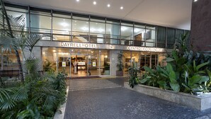 Entrada del DAYRELLHOTEL & CENTRO DE CONVENÇÕES con puertas de vidrio, un camino de baldosas y follaje circundante.