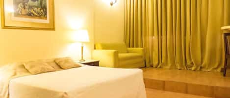 A hotel room with a bed, a chair, a lamp, and a painting on the wall.