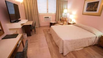 Quarto de hotel com cama, escrivaninha, cadeira, televisão e um quadro na parede.