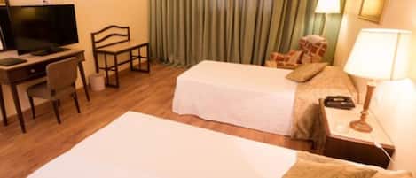 A hotel room with two beds, a desk with a television, a chair, and a lamp.