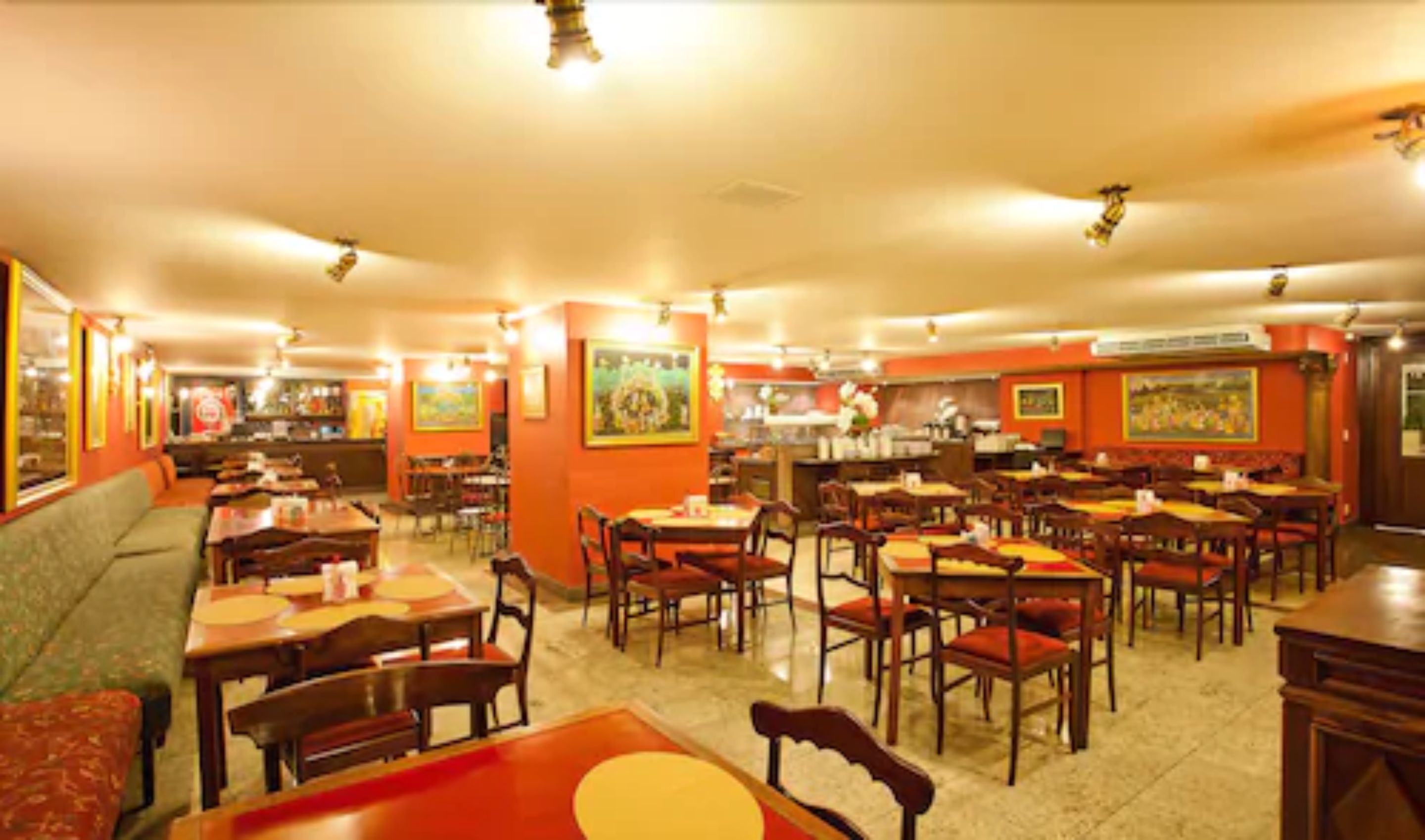Un restaurant doté de plusieurs tables et chaises, d’un espace cuisine et d’un coin salon avec un canapé.