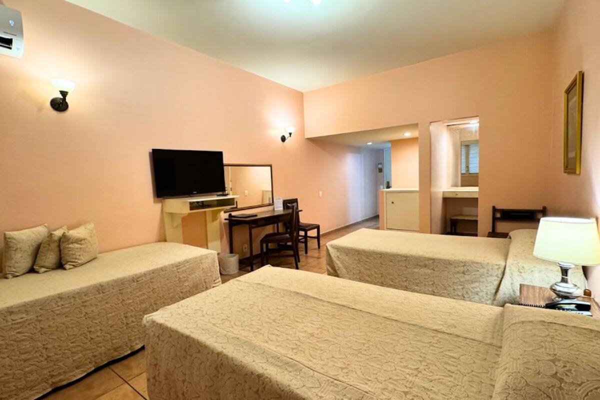 Hotellihuone, jossa on kaksi sänkyä, televisio, työpöytä ja pieni keittiönurkkaus.