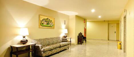 Um hall de hotel com um sofá, duas luminárias, um quadro e uma porta ao fundo.