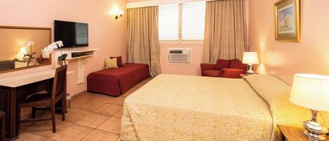Habitación de hotel con cama, escritorio con silla, televisor, ventana con cortinas e imagen enmarcada en la pared.