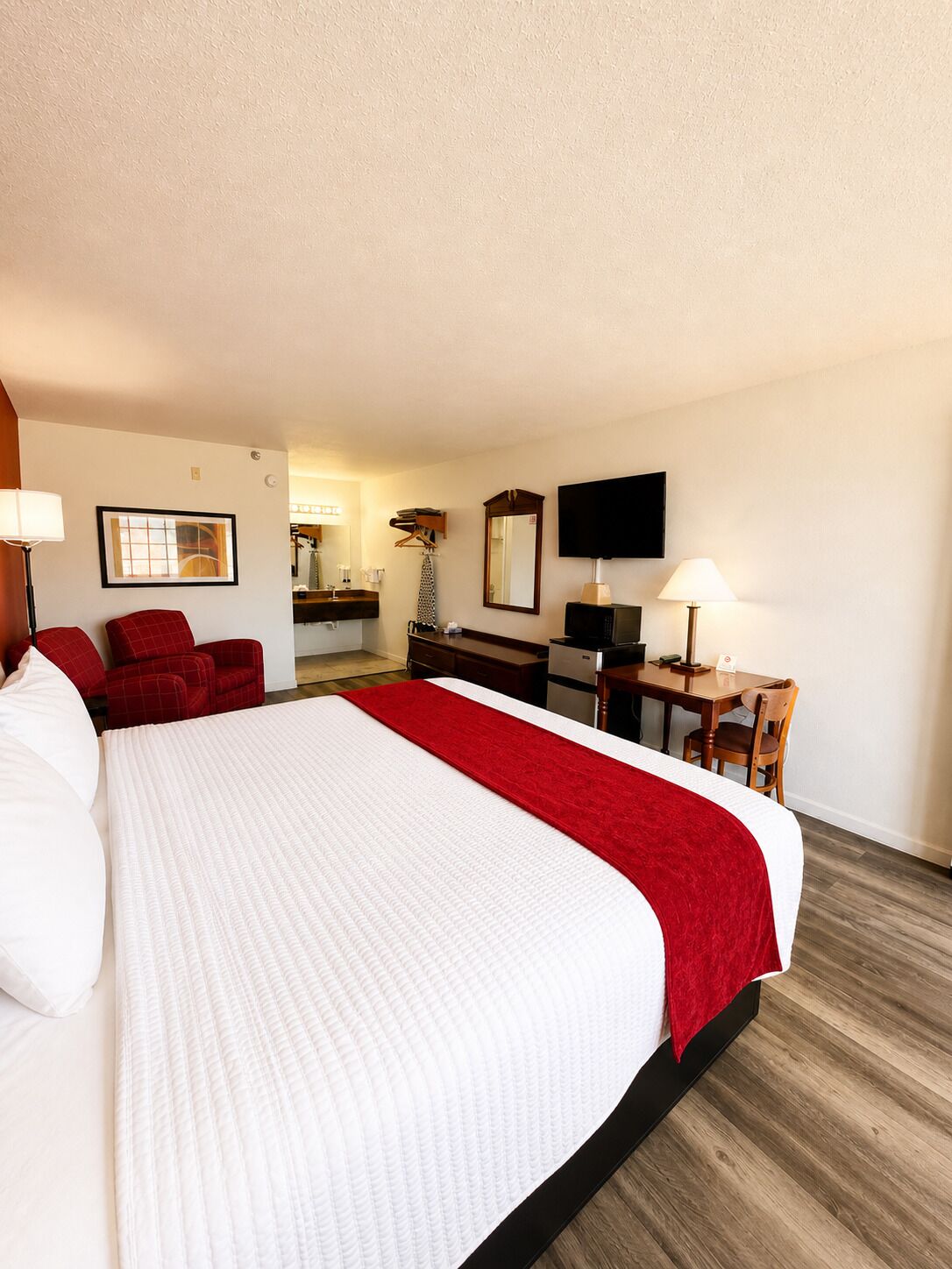 A hotel room with a large bed, a desk, a chair, a television, and a mirror.
