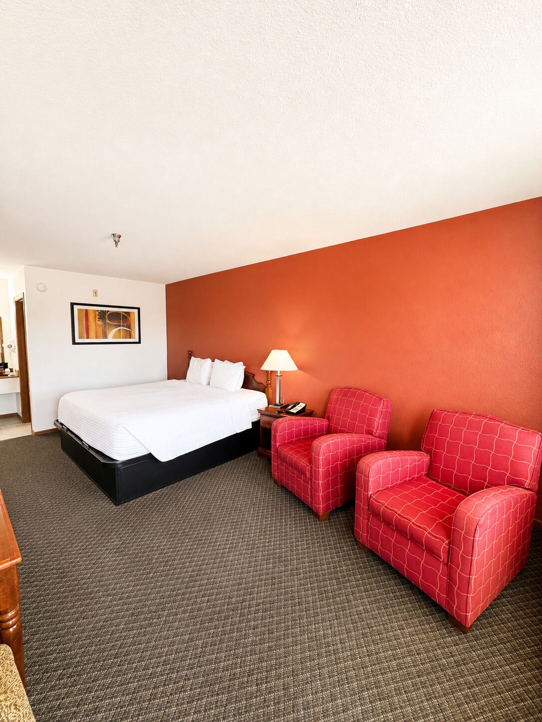Een hotelkamer met een bed, een rode fauteuil, een lamp en een ingelijst kunstwerk aan de muur.