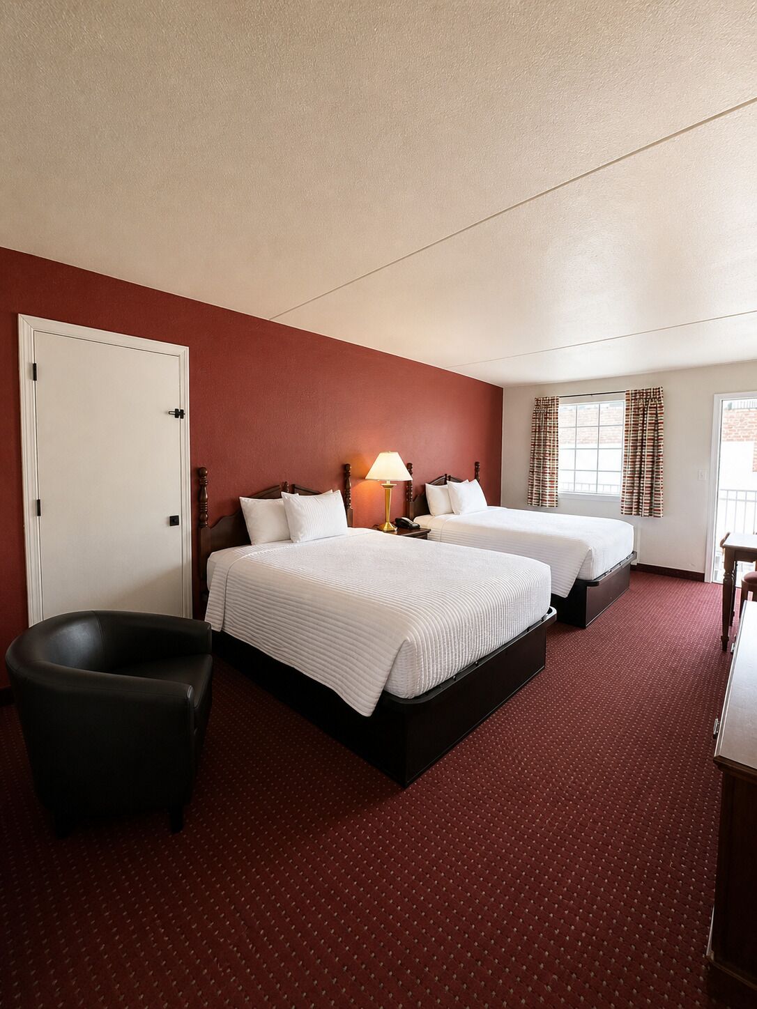 Une chambre d’hôtel avec deux lits, un bureau, une chaise et une fenêtre avec des rideaux.