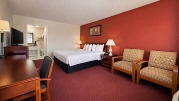 A hotel room with a bed, two armchairs, a desk, a television, and a painting on the wall.