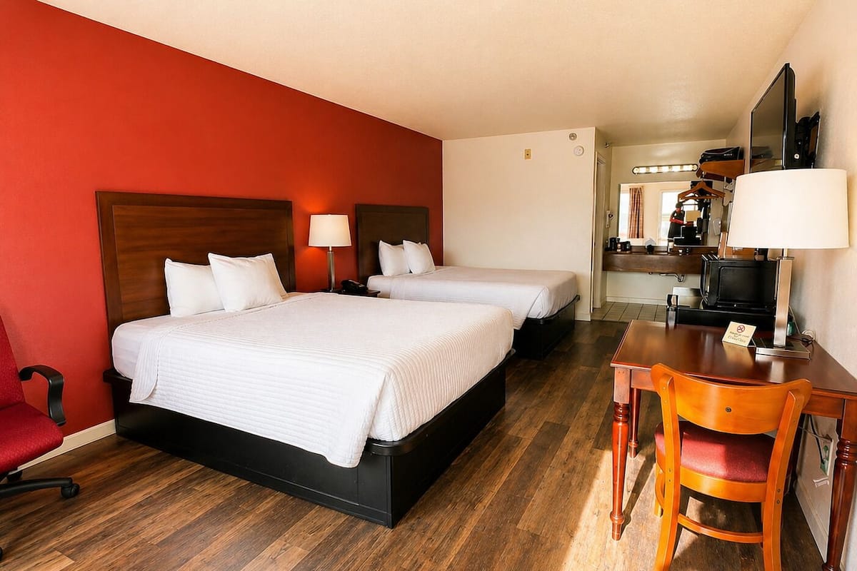 A hotel room with two beds, a desk, a chair, a mirror, and a television.