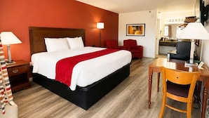 A hotel room with a bed, a desk, a chair, a TV, and a mirror. - Carriage House Inn (Branson)