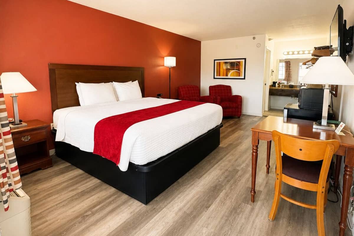 A hotel room with a bed, a desk, a chair, a TV, and a mirror.