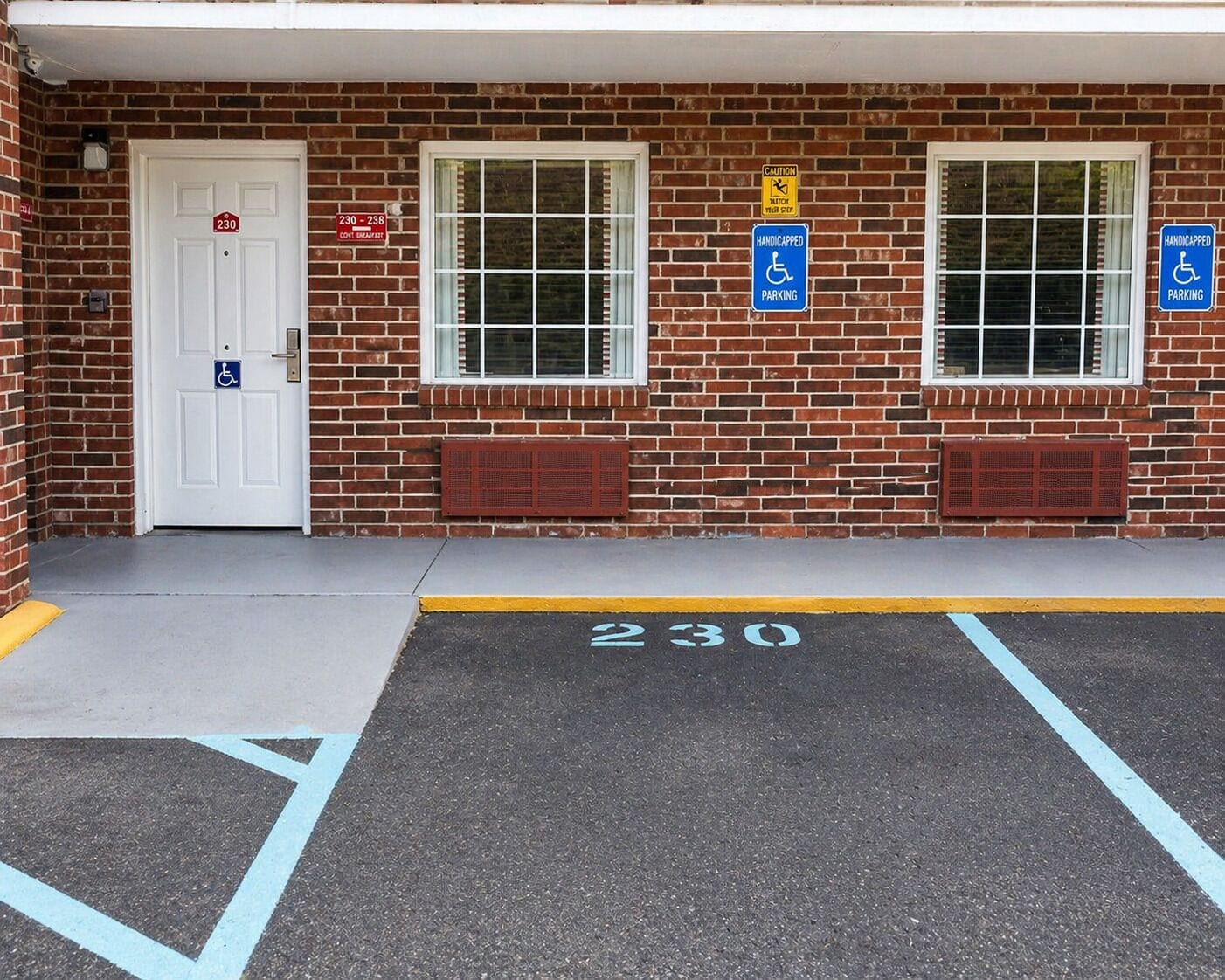 A building with a brick facade, two windows, a door with a handicap parking sign, and a parking space marked '230'.