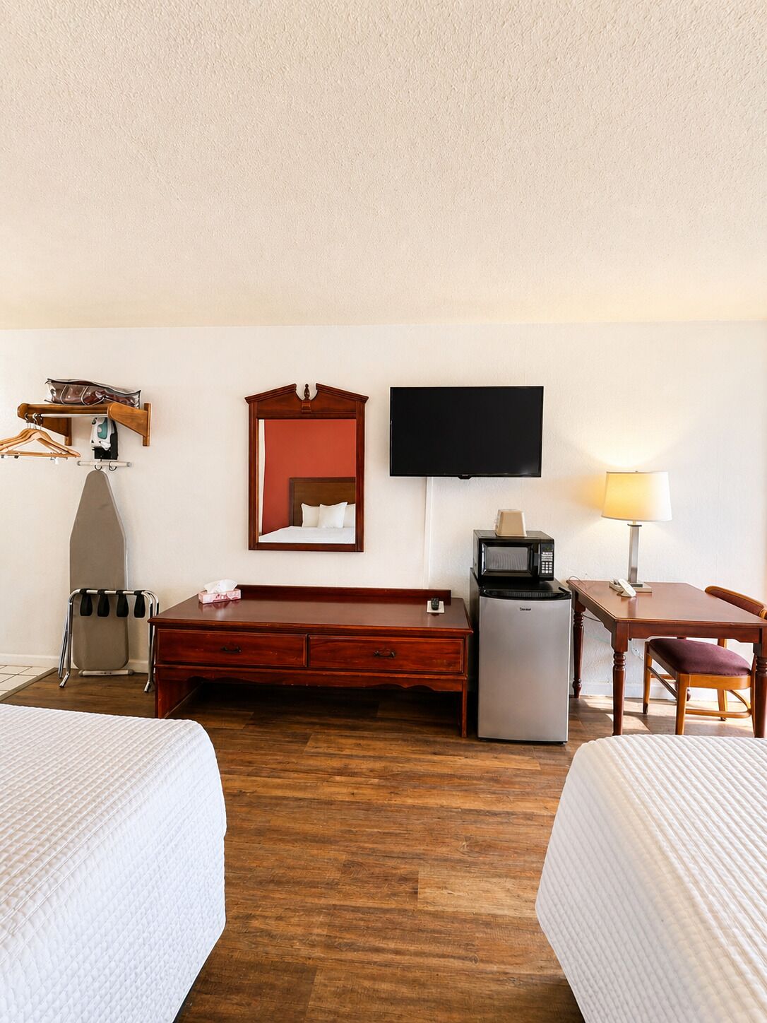 A hotel room with two beds, a desk, a television, a refrigerator, and a mirror.