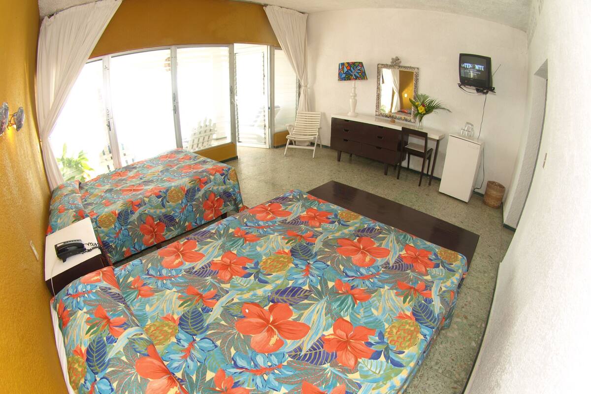 A hotel room with two beds, a desk, a chair, a TV, and a window with curtains.