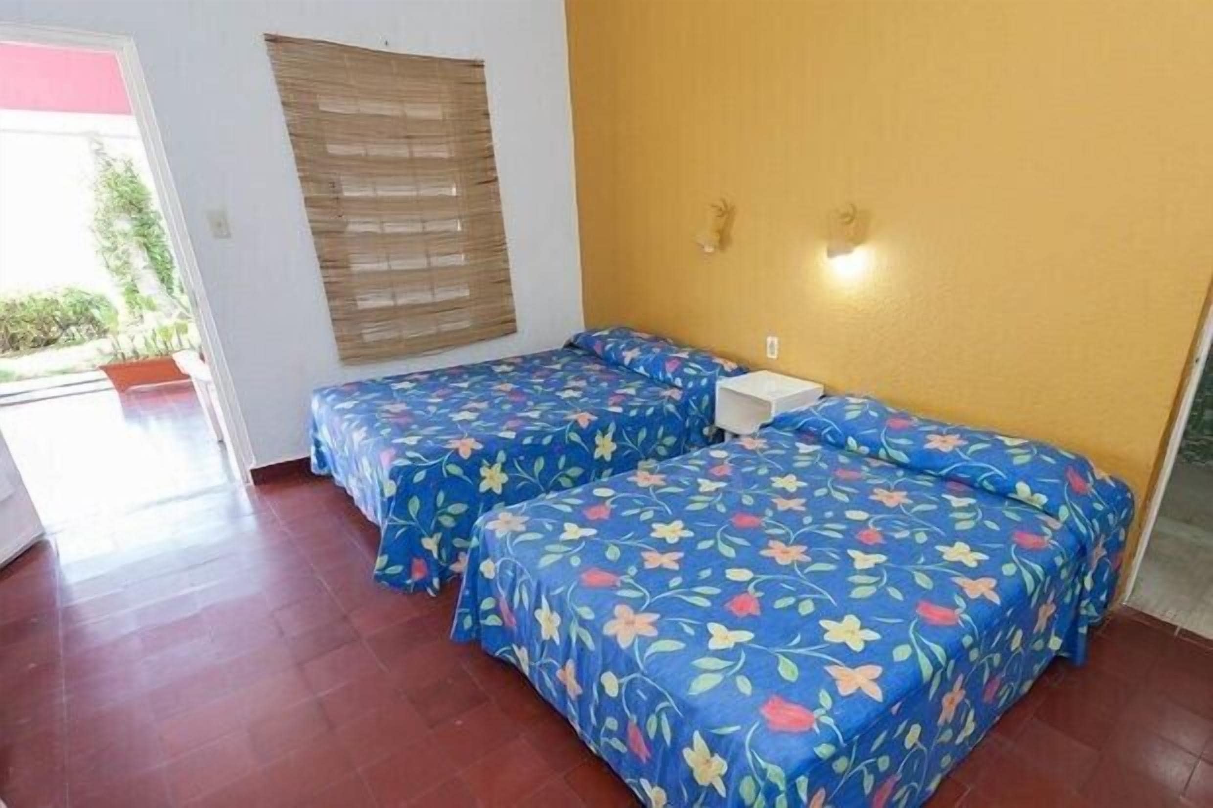 Una habitación con dos camas, cabecero de madera, una mesita de noche y una ventana con persianas.