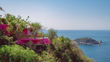 A pink building with a thatched roof overlooking a coastal area.