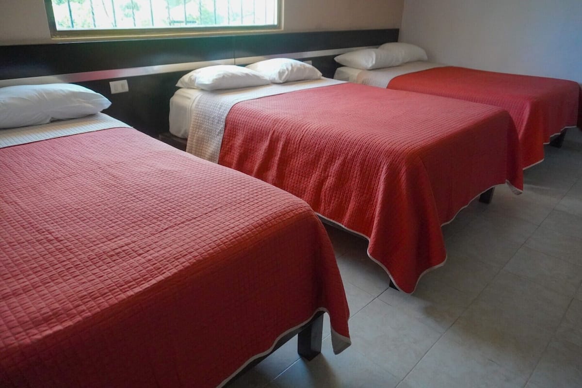 Habitación de hotel con tres camas individuales, cada una con cubrecama rojo y almohadas blancas.