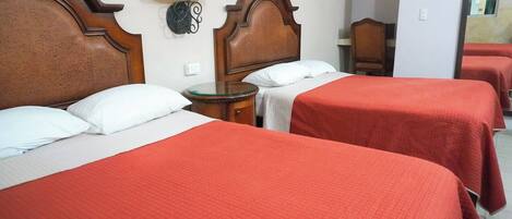 A hotel room with two beds, each with a red bedspread and white pillows. There is a wooden headboard, a bedside table with a lamp, and a mirror on the wall.