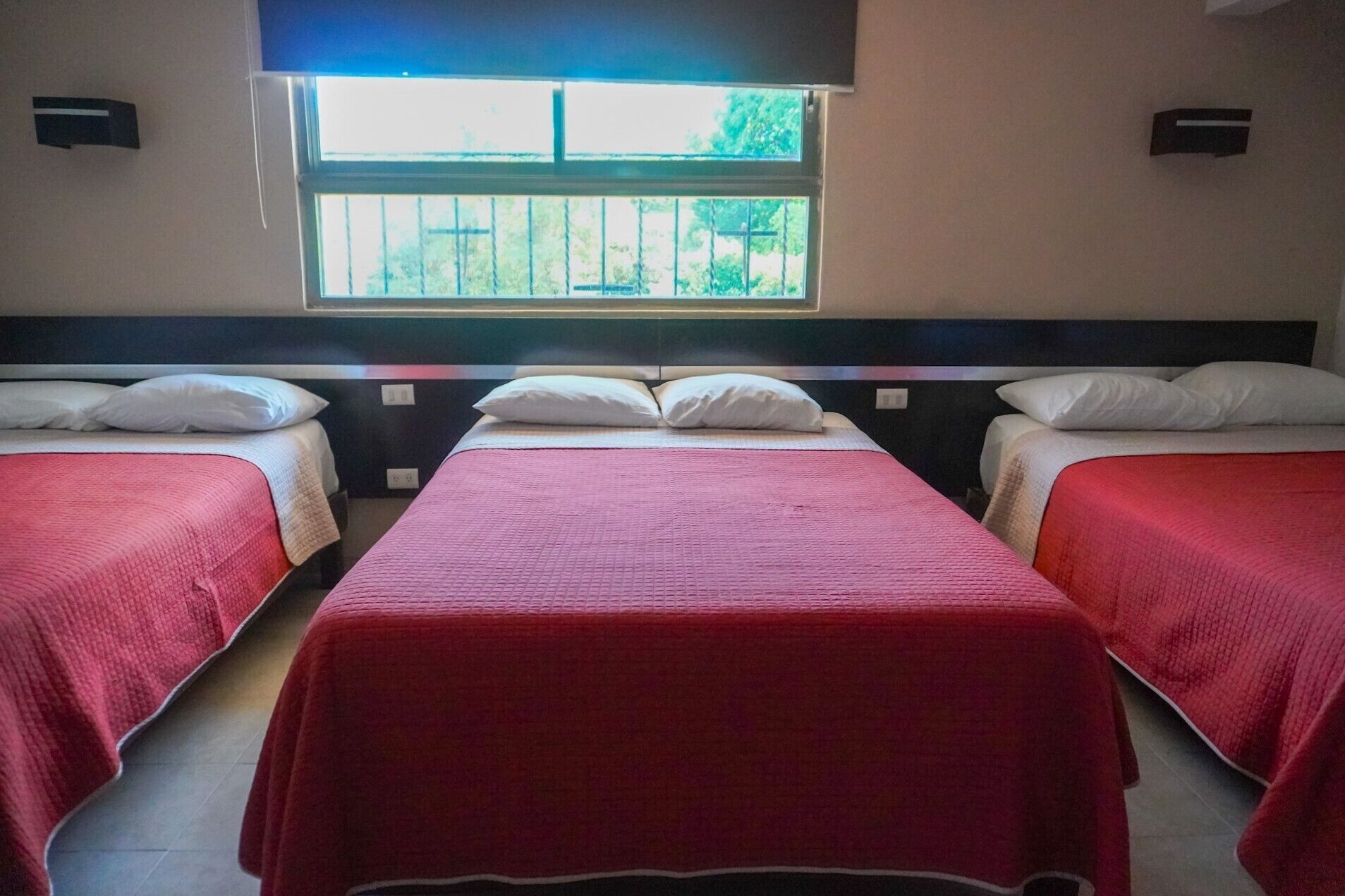 Une chambre d’hôtel avec deux lits simples, chacun recouvert d’une couverture rouge et agrémenté d’oreillers blancs. Une fenêtre située au-dessus des lits laisse entrer la lumière naturelle.
