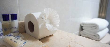 Un baño con encimera de mármol, un rollo de papel higiénico con un lazo decorativo y artículos de aseo que incluyen jabón y loción.