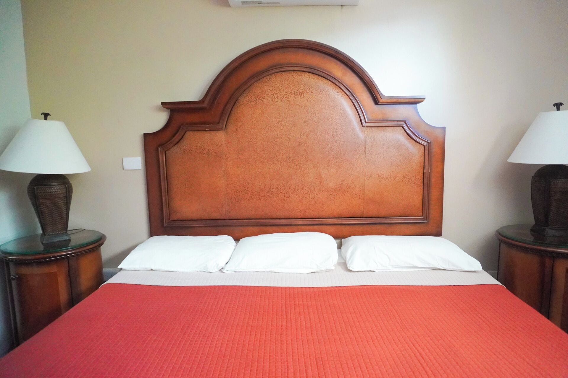 A hotel room with a large bed, a red bedspread, two bedside lamps, and a wooden headboard.