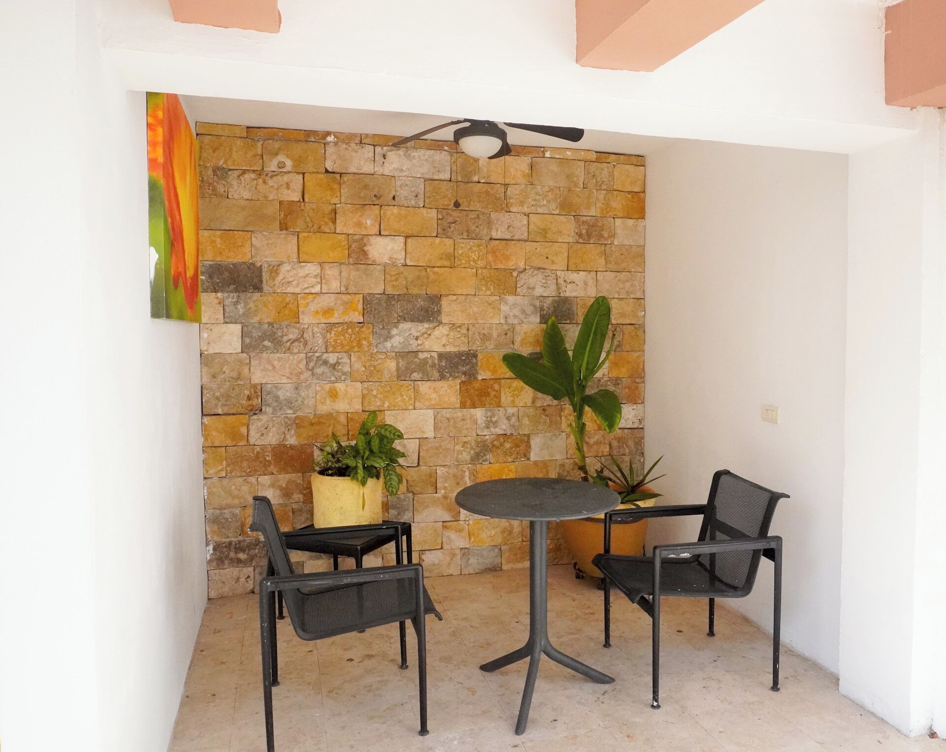 A small, enclosed patio area with a stone wall, two chairs, a table, and two potted plants.