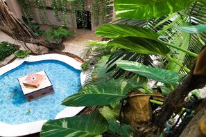 A circular pool with a small structure in the center, surrounded by lush greenery and a building with a door in the background. - Hotel Colonial Cancun (Cancun)