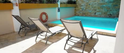 Un área de piscina con sillones de descanso y un muro de ladrillo.