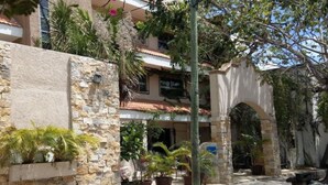 A courtyard with stone walls, potted plants, and an archway leading to a building with a tiled roof. - Hotel Colonial Cancun (Cancun)
