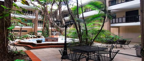Un patio con piscina, mobiliario exterior y abundante vegetación.