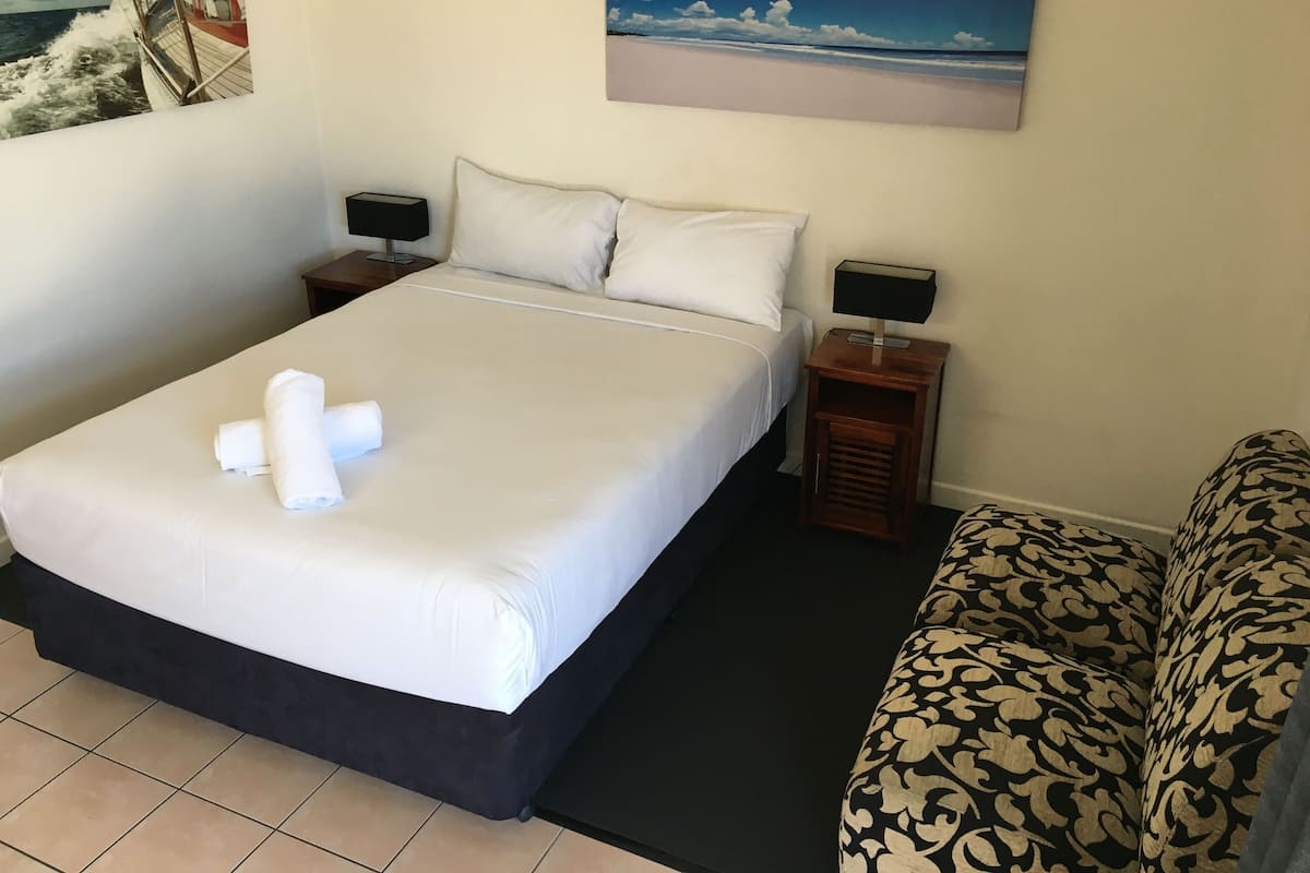 Una habitación de hotel con una cama grande, dos mesitas de noche con lámparas, un sofá estampado y dos cuadros colgados en la pared.