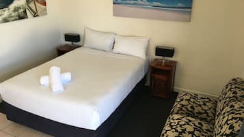 A hotel room with a large bed, two bedside tables with lamps, a patterned sofa, and two wall-mounted paintings.