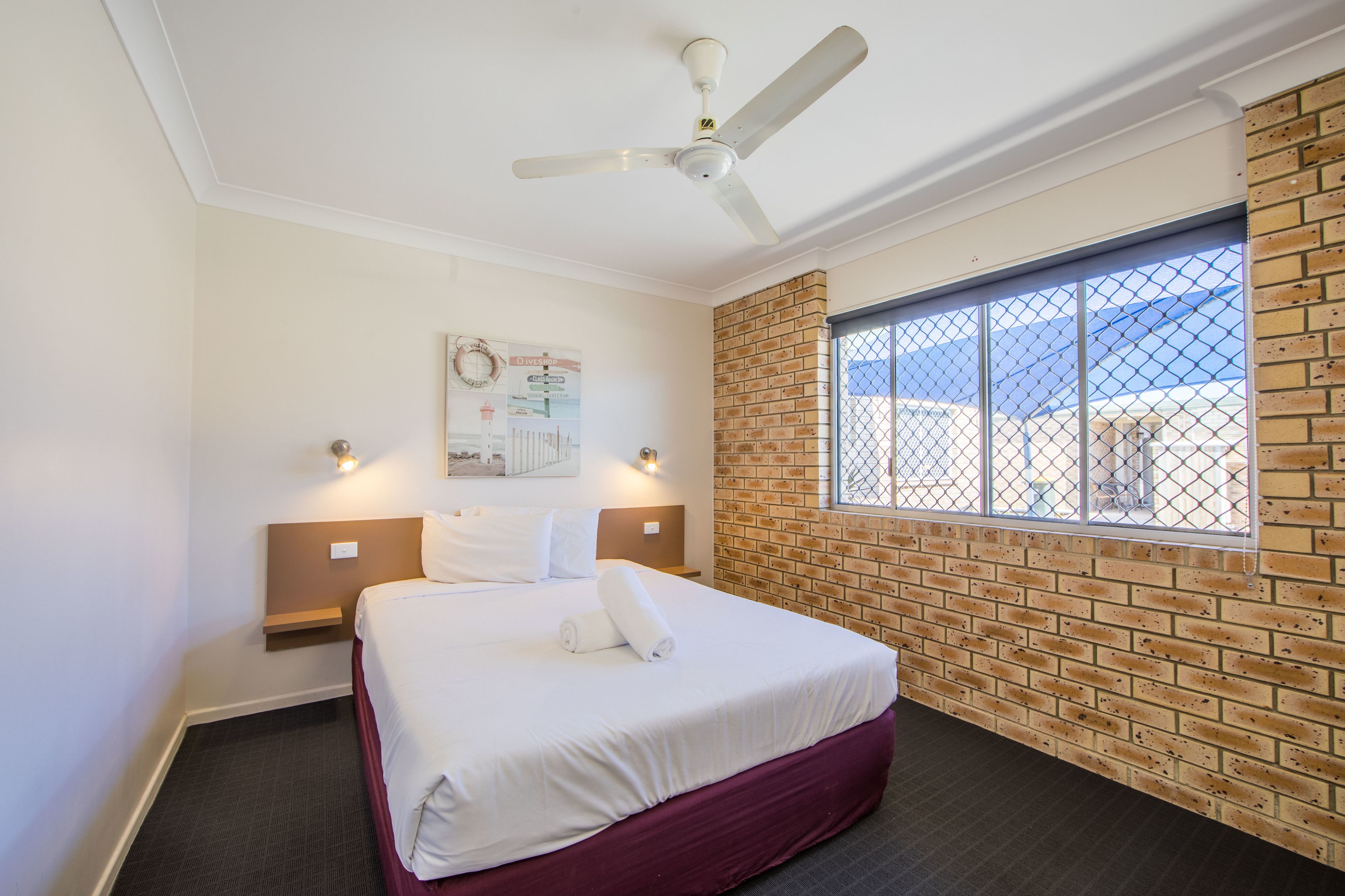 Une chambre d’hôtel avec un lit, un ventilateur de plafond, une fenêtre donnant sur un paysage agréable et un mur en briques.