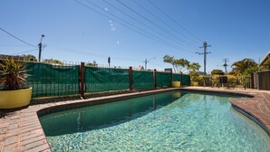 En klar swimmingpool med murstenskanter, omgivet af et grønt hegn og plantekasser.