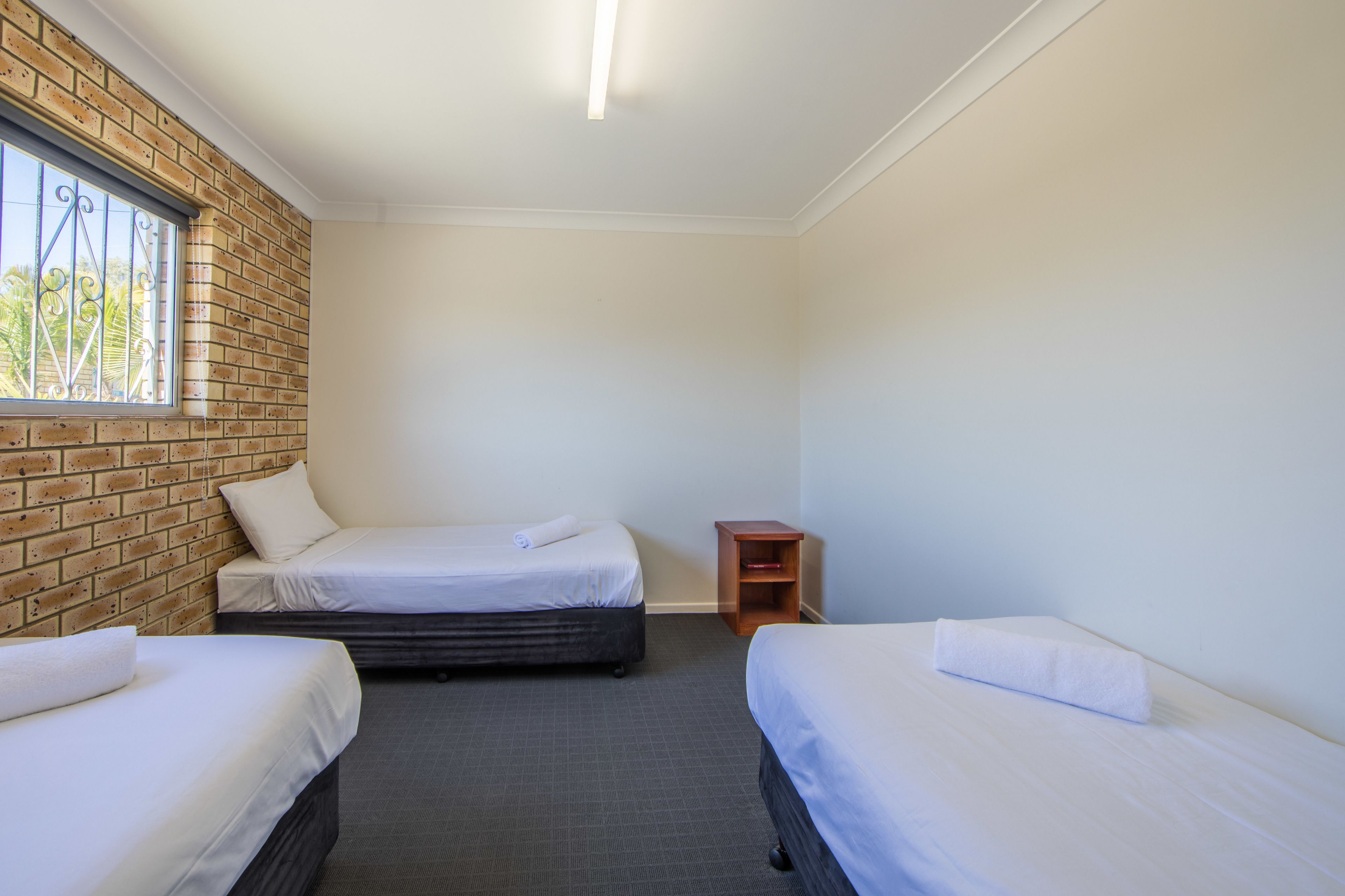 A room with two beds, a brick wall, a window, and a small wooden nightstand.