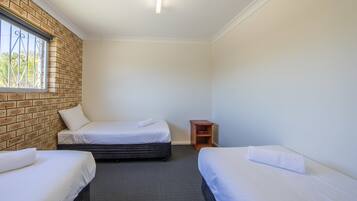 A room with two beds, a brick wall, a window, and a small wooden nightstand.