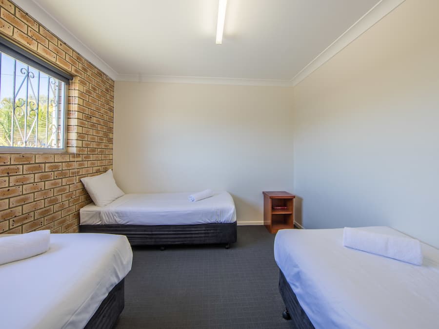 A room with two beds, a brick wall, a window, and a small wooden nightstand.