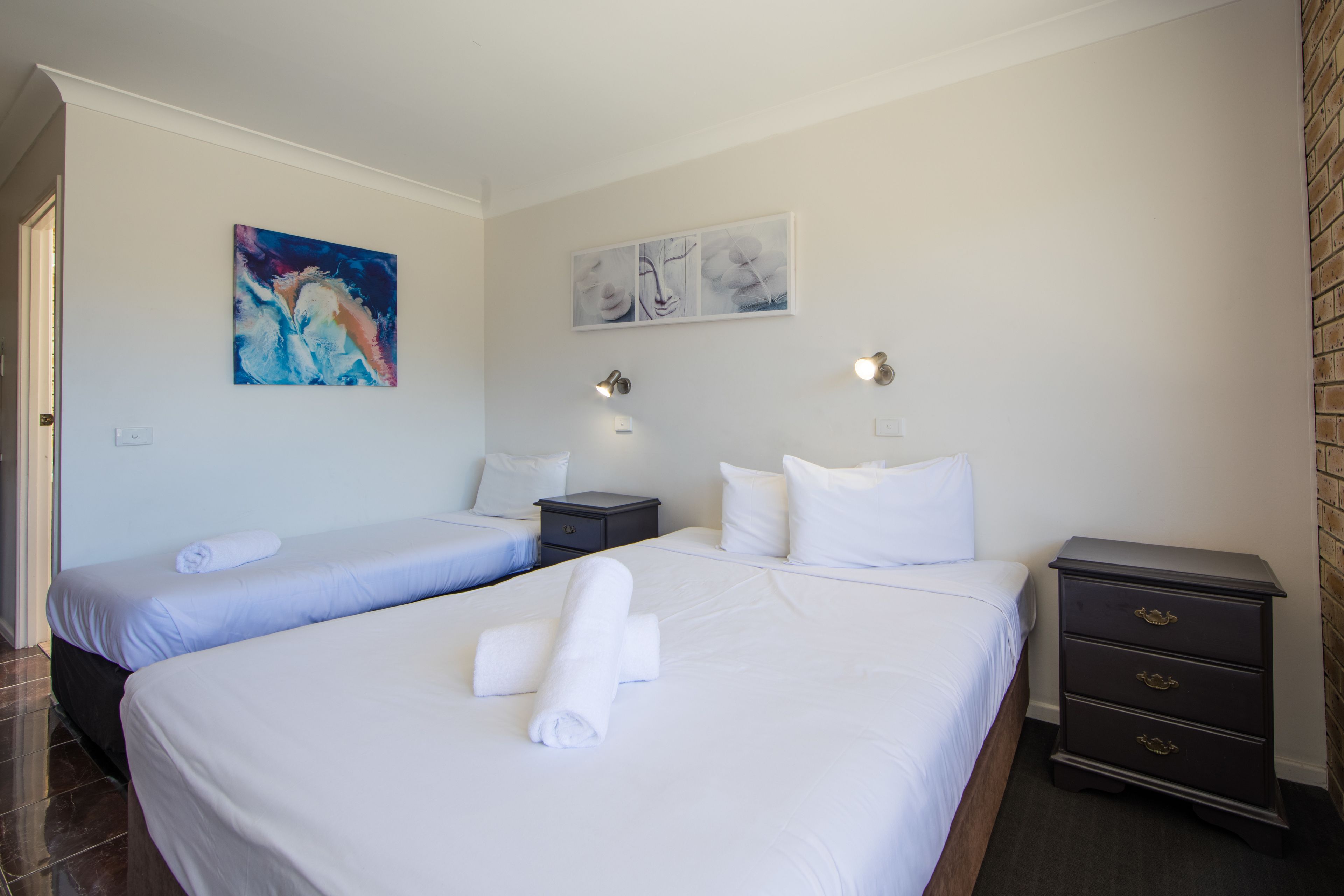 A hotel room with two beds, a nightstand, and artwork on the walls.