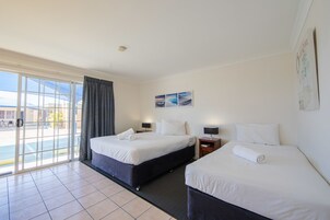 Habitación de hotel con dos camas, un ventanal con cortinas, una mesita de noche con lámpara y una pared con tres cuadros enmarcados.